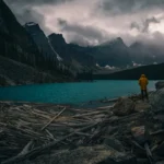 a person in a yellow jacket standing on rocks near a body of water