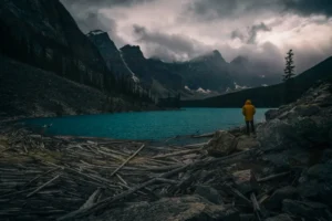 a person in a yellow jacket standing on rocks near a body of water