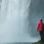 man standing on a rock facing waterfalls