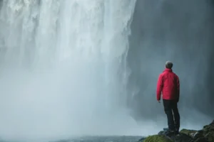 man standing on a rock facing waterfalls