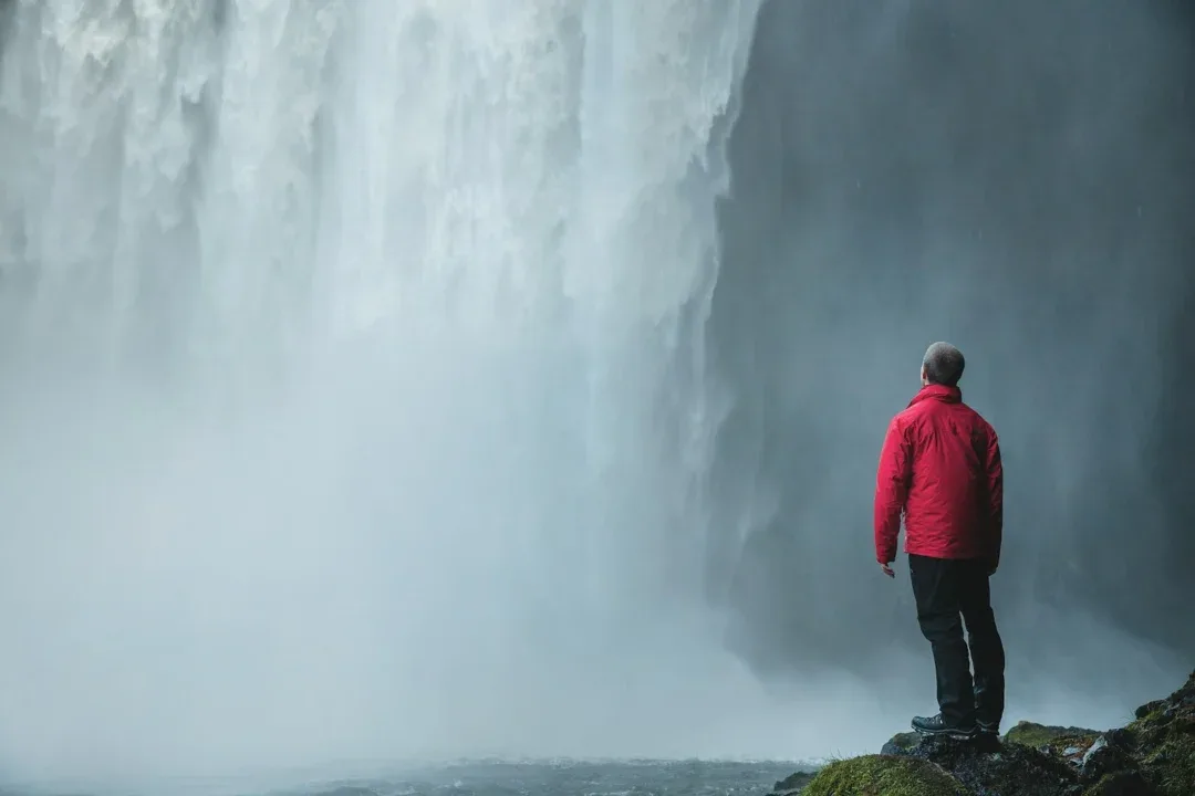 man standing on a rock facing waterfalls